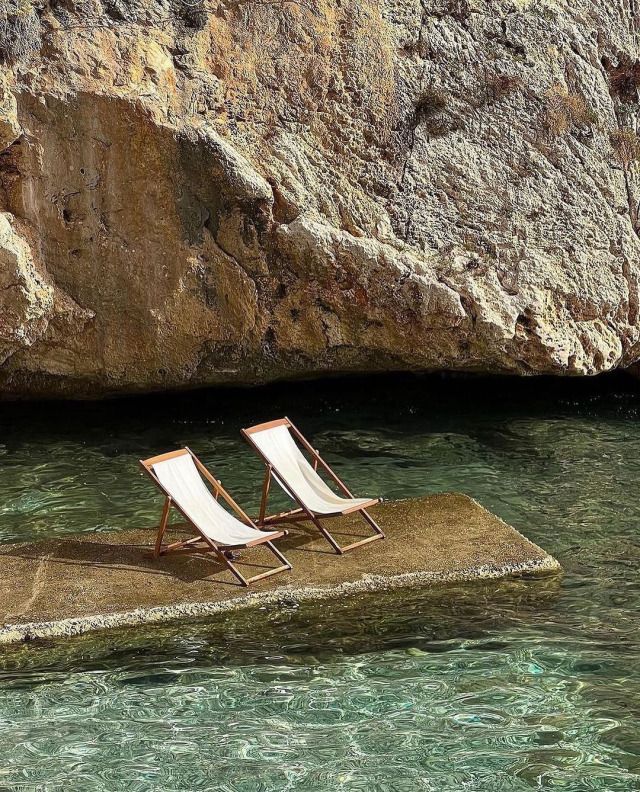 Two lounge chairs on a rock platform in emerald water